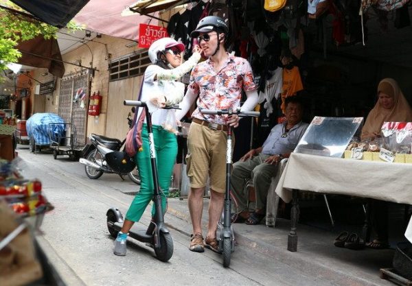 Two people on scooters, one feeding the other food.