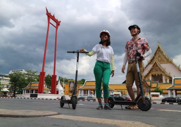 Two people with electric scooter behind the Giant Swing Bangkok